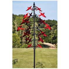 a tall metal sculpture with red flowers on it's side in the middle of a field