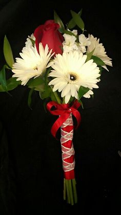 a bouquet of white and red flowers tied to a ribbon with a rose in the background