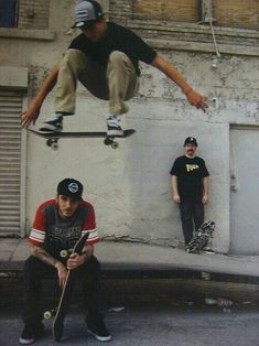 two men are doing tricks on skateboards in front of a building and another man is sitting down