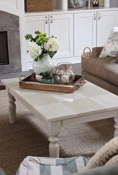 a white coffee table with flowers in a vase on it and a tray full of candles