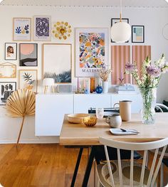 a dining room table and chairs with pictures on the wall above it, along with vases filled with flowers