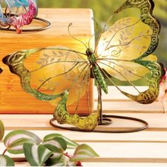 two glass butterflies sitting on top of a wooden box next to some plants and flowers