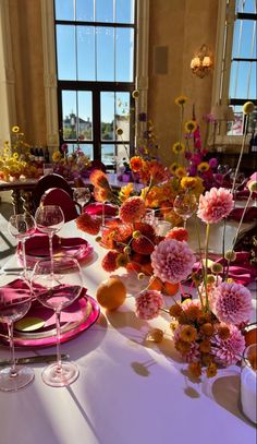 the table is set with plates, glasses and vases filled with different colored flowers