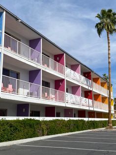 an apartment building with colorful balconies and palm trees in the parking lot next to it