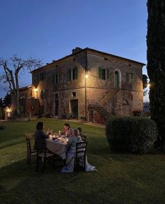 people are sitting at a table outside in front of an old building with lights on