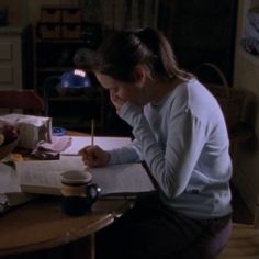 a woman sitting at a table writing on a piece of paper with a pen in her hand