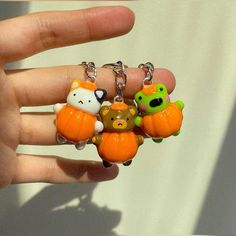 a hand holding three small keychains with animals on them and pumpkins in the background