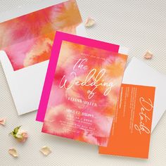 the wedding stationery is laid out on top of each other, with pink and orange watercolors