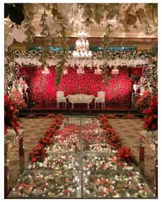 a room filled with lots of red flowers and greenery next to a chandelier