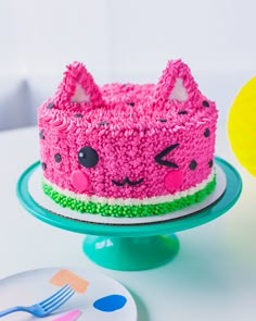 a cake with pink frosting and cat ears on it sitting on a plate next to a fork