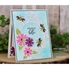 a close up of a card with flowers and bees on it, in front of a wooden background