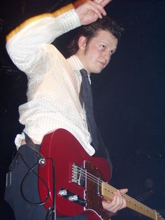 a young man holding a red guitar in his right hand