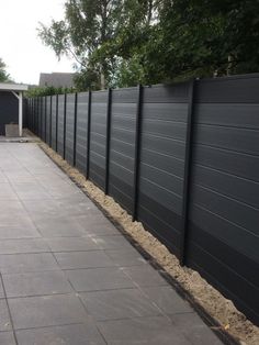 a long black fence is next to a paved area in the back yard with trees