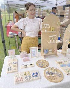 a woman standing next to a table full of wooden crafts and decorations on it's sides