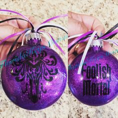 two purple ornaments with black writing on them, one is being held by a hand