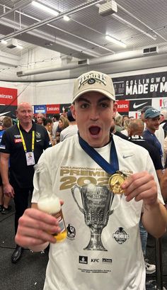 a young man holding a trophy in his right hand and wearing a white shirt with a gold medal around his neck