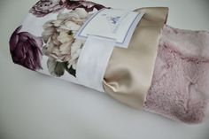 a pink flowered blanket folded up on top of a white tablecloth with a tag