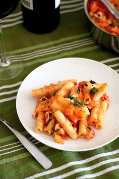 a white plate topped with pasta next to a bottle of wine and two silverware