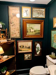 a bathroom with green walls and pictures on the wall above the toilet, along with a white sink