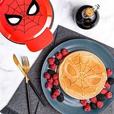 a pancake with berries on the side and a spiderman face plate next to it