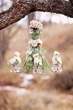 a chandelier hanging from a tree with flowers and greenery in the center