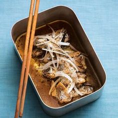 a pan filled with meat and onions next to chopsticks on a blue surface