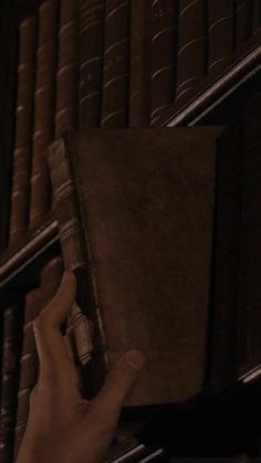 a hand is holding an old book in front of a row of bookshelves