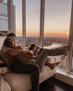 a woman sitting on top of a couch in front of a window next to a tall building