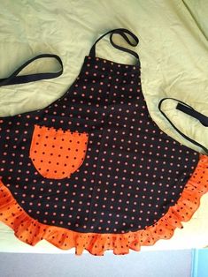 a black and orange polka dot apron with an orange ruffle on the bottom, sitting on a bed