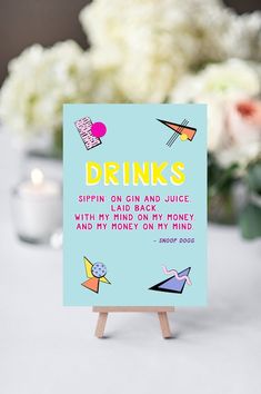 a card that says drinks on it sitting on a table with flowers in the background