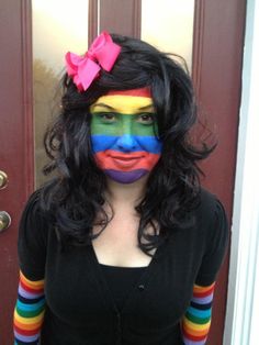 a woman with her face painted like a clown wearing a rainbow striped shirt and pink bow