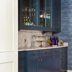 a kitchen with blue cabinets and marble counter tops, along with wine glasses on the cabinet doors