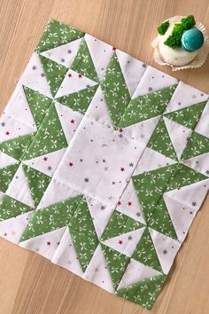 a green and white quilt next to a cupcake on a wooden table with an ornament