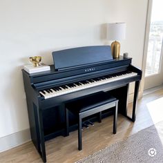 a black piano sitting in front of a window next to a table with a lamp on it