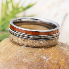 two wedding bands with wood inlays on top of a rock next to a plant