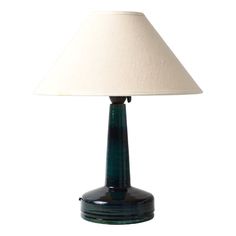 a green table lamp with a white shade on the base and a black vase underneath it