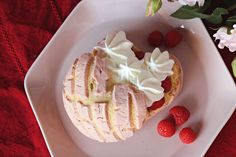 a heart shaped pastry with whipped cream and raspberries on a plate next to flowers