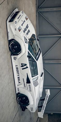 an aerial view of a white race car parked in front of a garage door with two signs on it