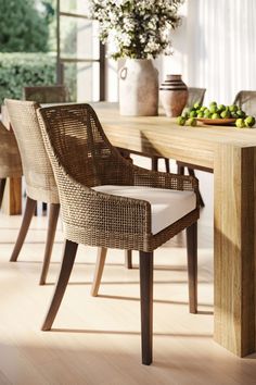 a dining room table and chairs with fruit on the table next to it in front of an open window