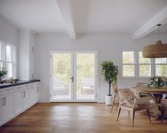 a kitchen with white walls and wooden floors has an open door leading to the outside