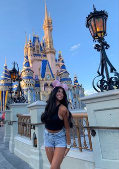 a woman standing in front of a castle at disney world with her pink hat on