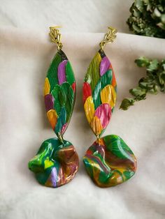 two pairs of colorful earrings sitting on top of a white cloth next to a plant