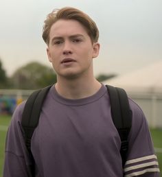 a young man with a backpack on his back standing in front of a soccer field