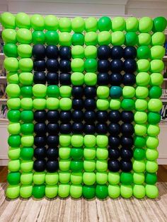 a large green and black letter made out of balloons on top of a wooden floor