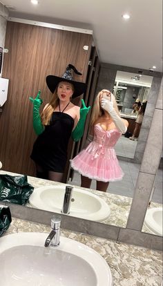 a woman in a pink dress and black hat taking a selfie in a bathroom mirror