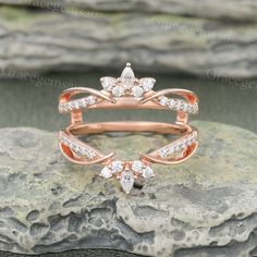 a rose gold ring set with diamonds on top of a large rock in front of some rocks