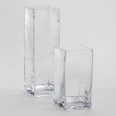 two clear vases sitting next to each other on a white surface with no one in it