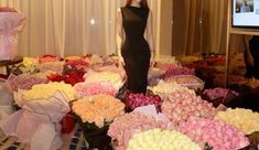 a woman in a black dress standing next to a large amount of flowers on display