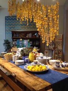 a wooden table topped with plates and bowls filled with lemons next to a yellow chandelier