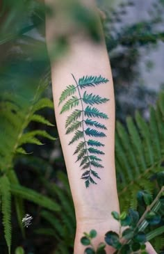 a fern leaf tattoo on the left forearm and hand, with green leaves around it